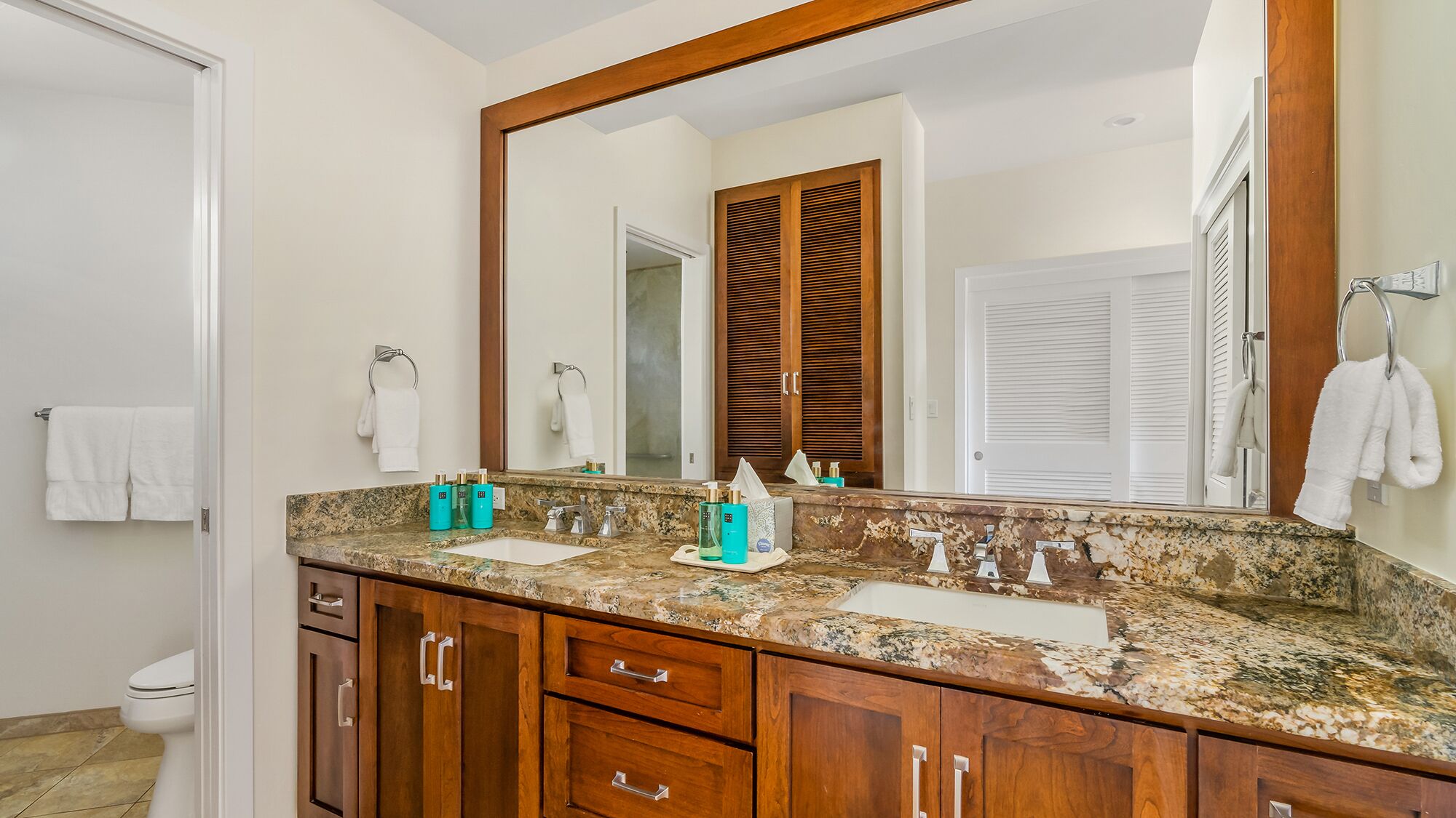A bathroom with a granite countertop, wooden cabinets, a large mirror, and two sinks.