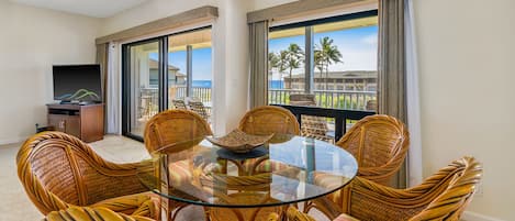 A round glass table surrounded by wicker chairs in a balcony area with a view of palm trees and a building.