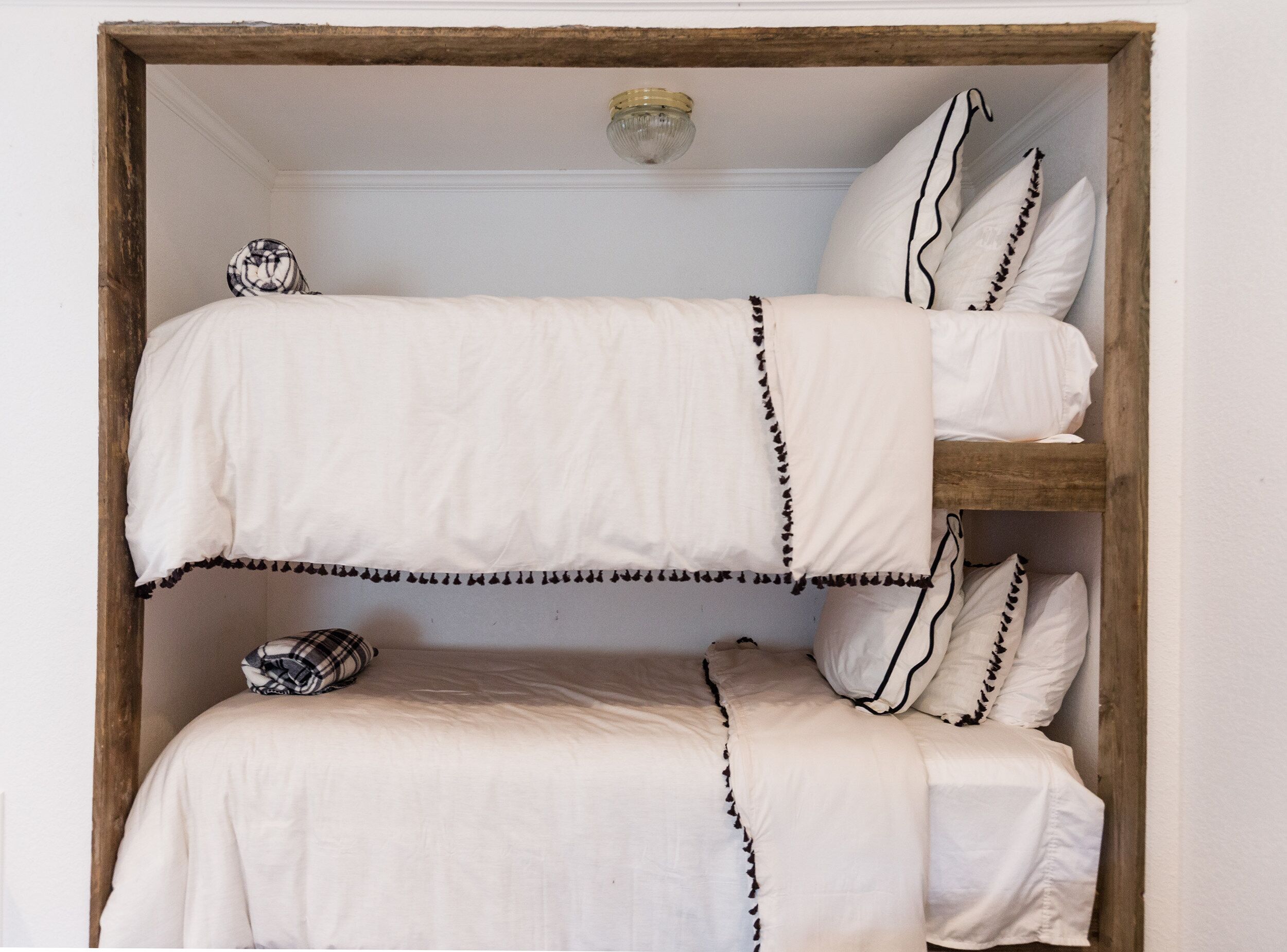 Un letto a castello con biancheria bianca e finiture nere, un tavolino rotondo e una lampada a sospensione.