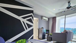 A modern living room with a sofa, a TV, a ceiling fan, and a large window with a view. - Sky Hive Cozy Apartment Suite, Georgetown (George Town)