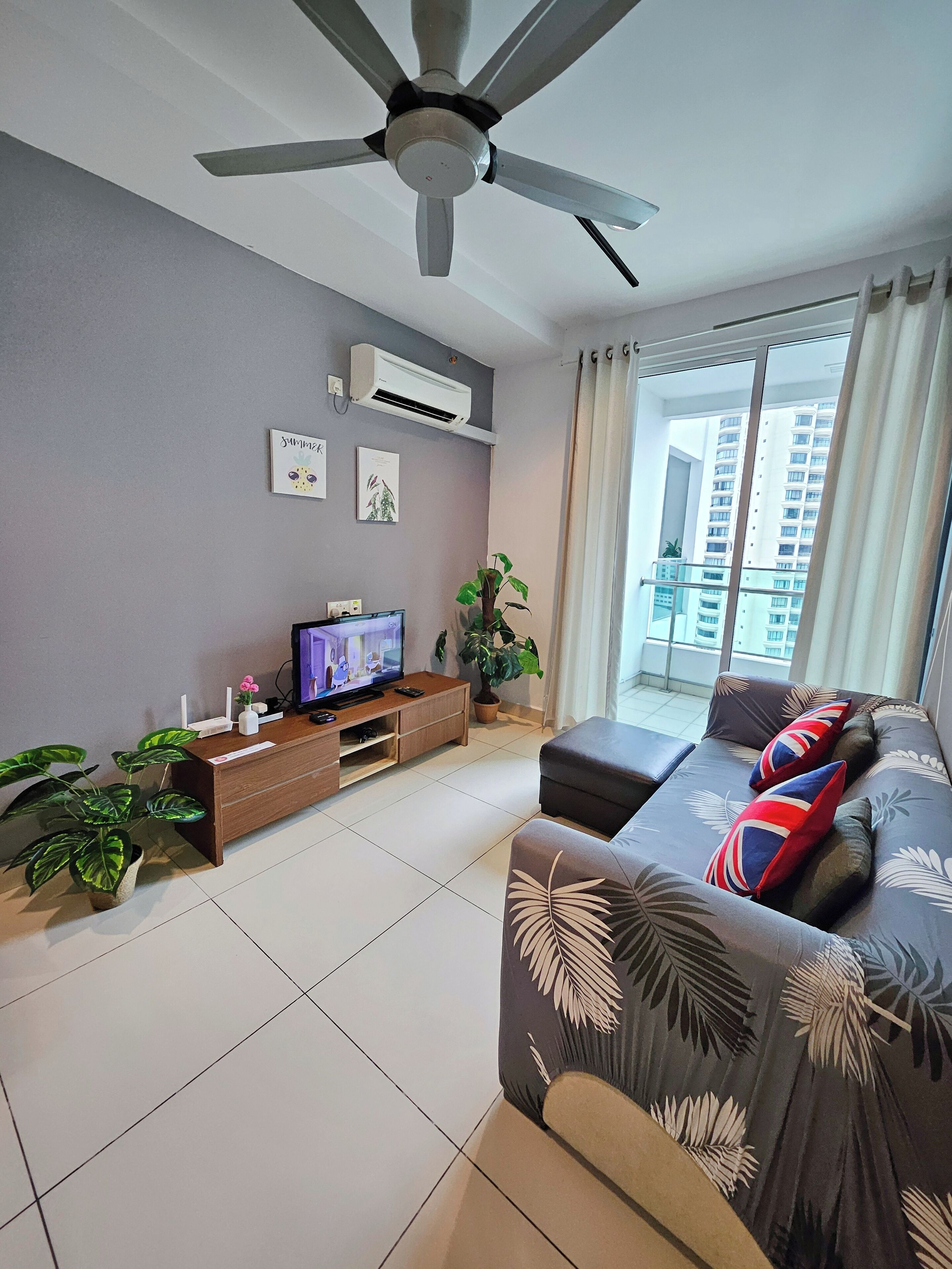 A modern living room with a ceiling fan, a flat-screen TV, a sofa with decorative pillows, a wooden entertainment unit, and a potted plant.
