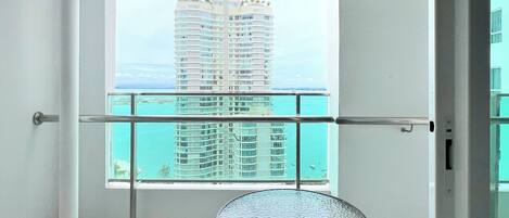 A balcony with two chairs and a small table, overlooking a high-rise building and a body of water.
