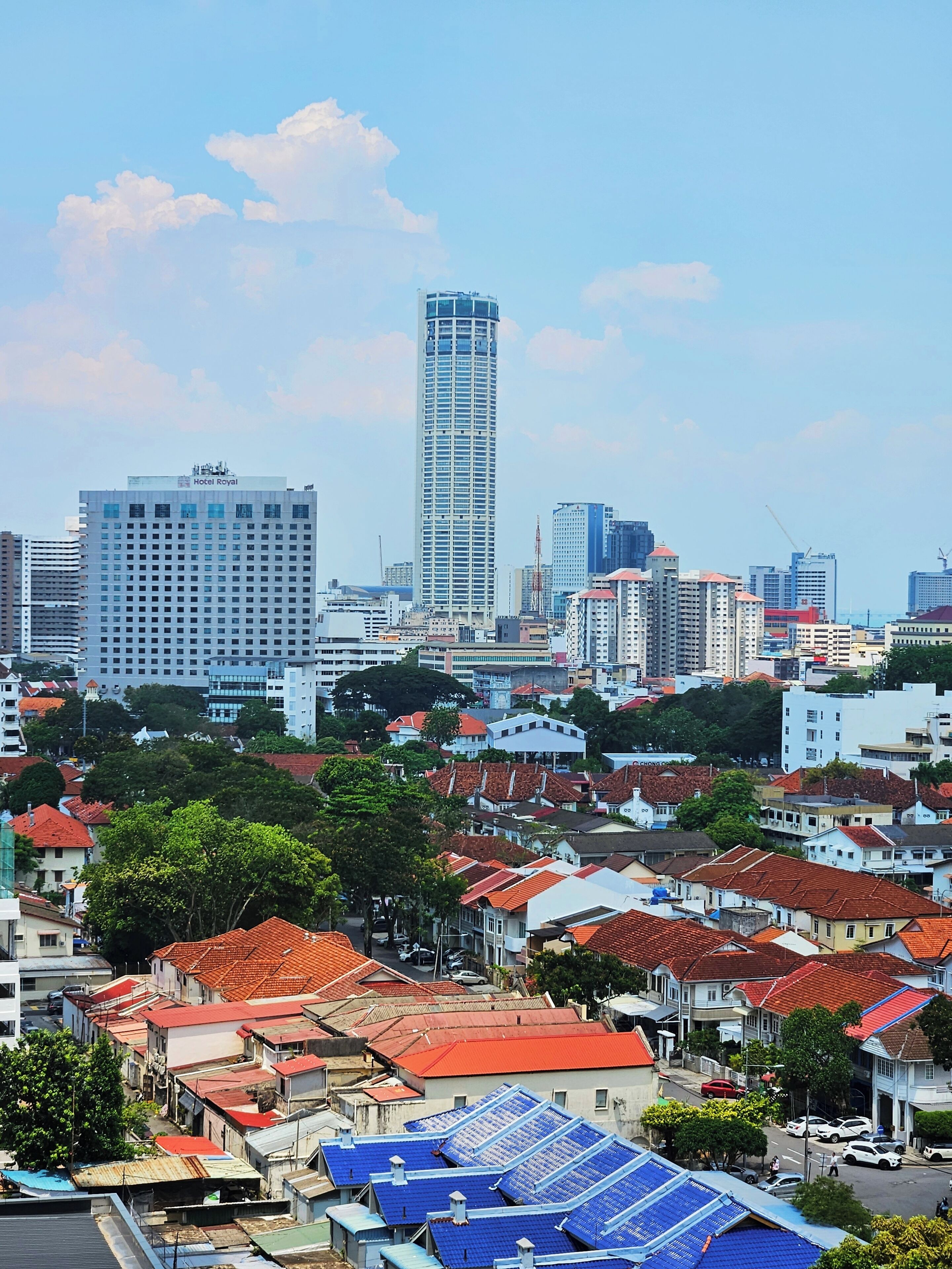 A cityscape with a prominent Hotel Royal building, surrounded by residential buildings with red-tiled roofs and a mix of modern and older architecture.