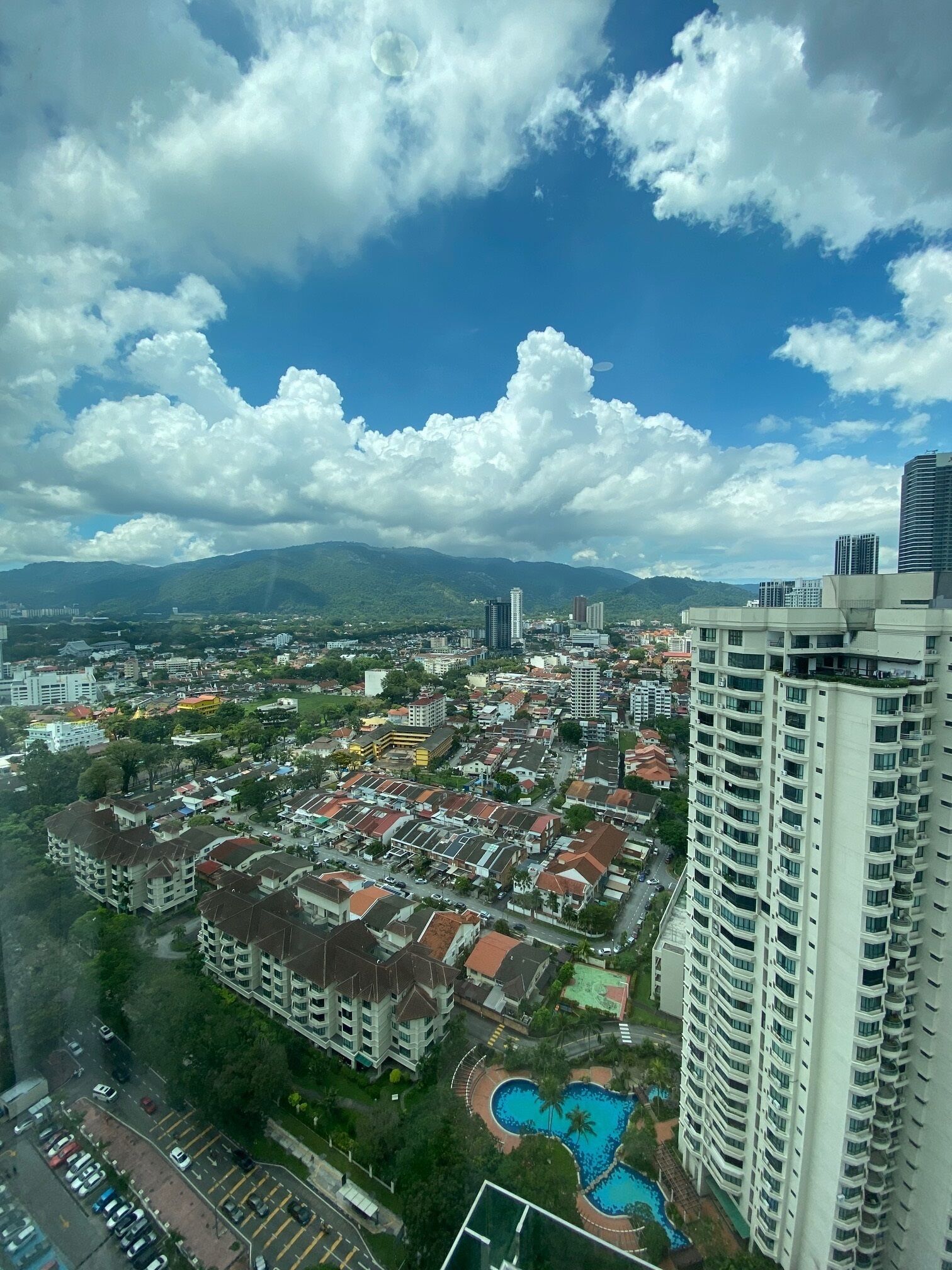 A high-rise building with a swimming pool and a view of a residential area with various buildings and a mountain in the background.