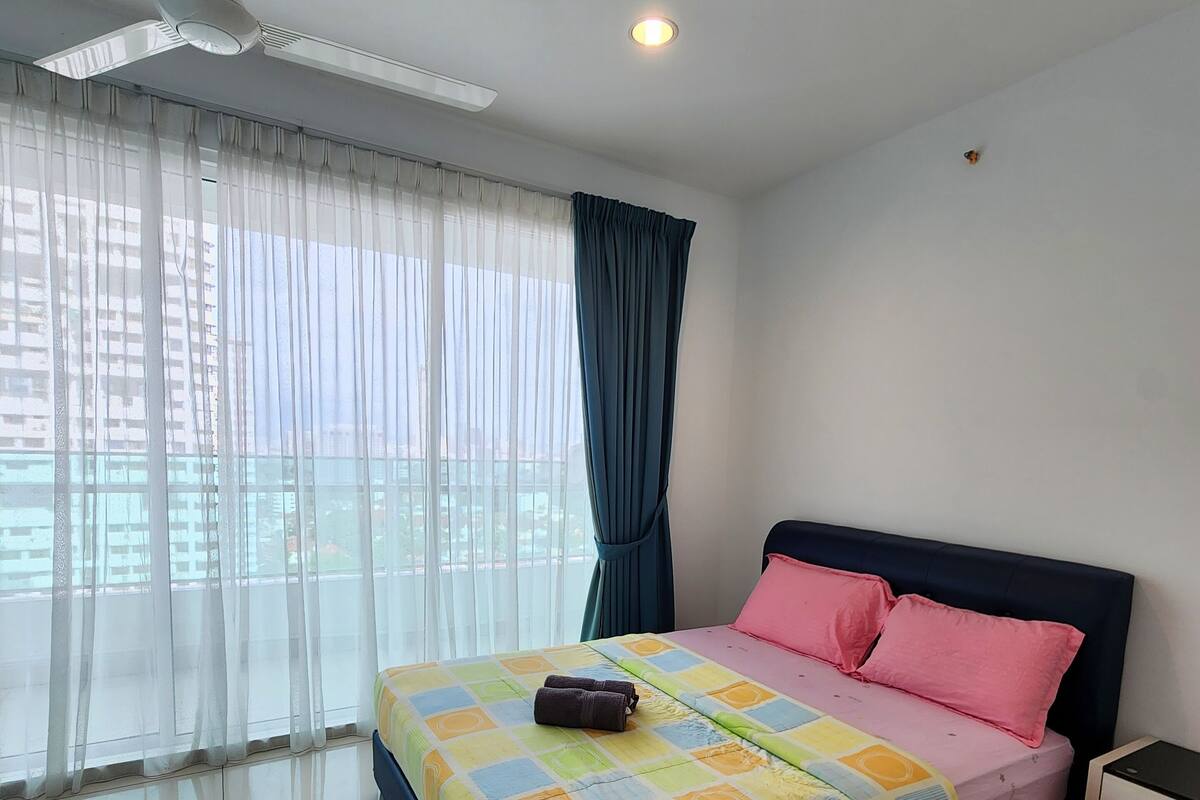 Ein Schlafzimmer mit Bett, Nachttisch, Deckenventilator und Fenster mit durchsichtigen Vorhängen.
