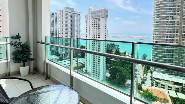 A balcony with a glass table and chairs, overlooking a cityscape with tall buildings and a clear sky. - Sky Hive Cozy Apartment Suite, Georgetown (George Town)
