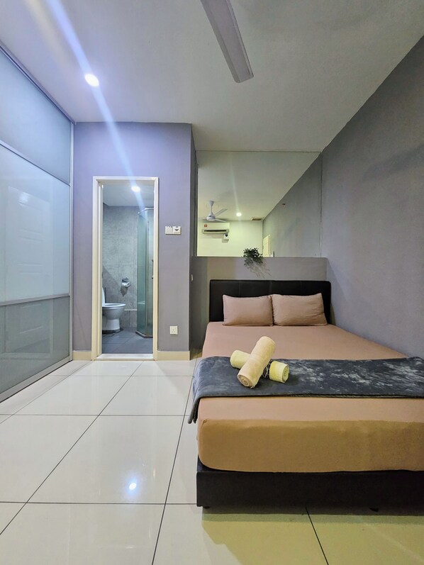 Un dormitorio moderno con cama, mesita de noche, ventilador de techo y baño visible a través de una puerta abierta.