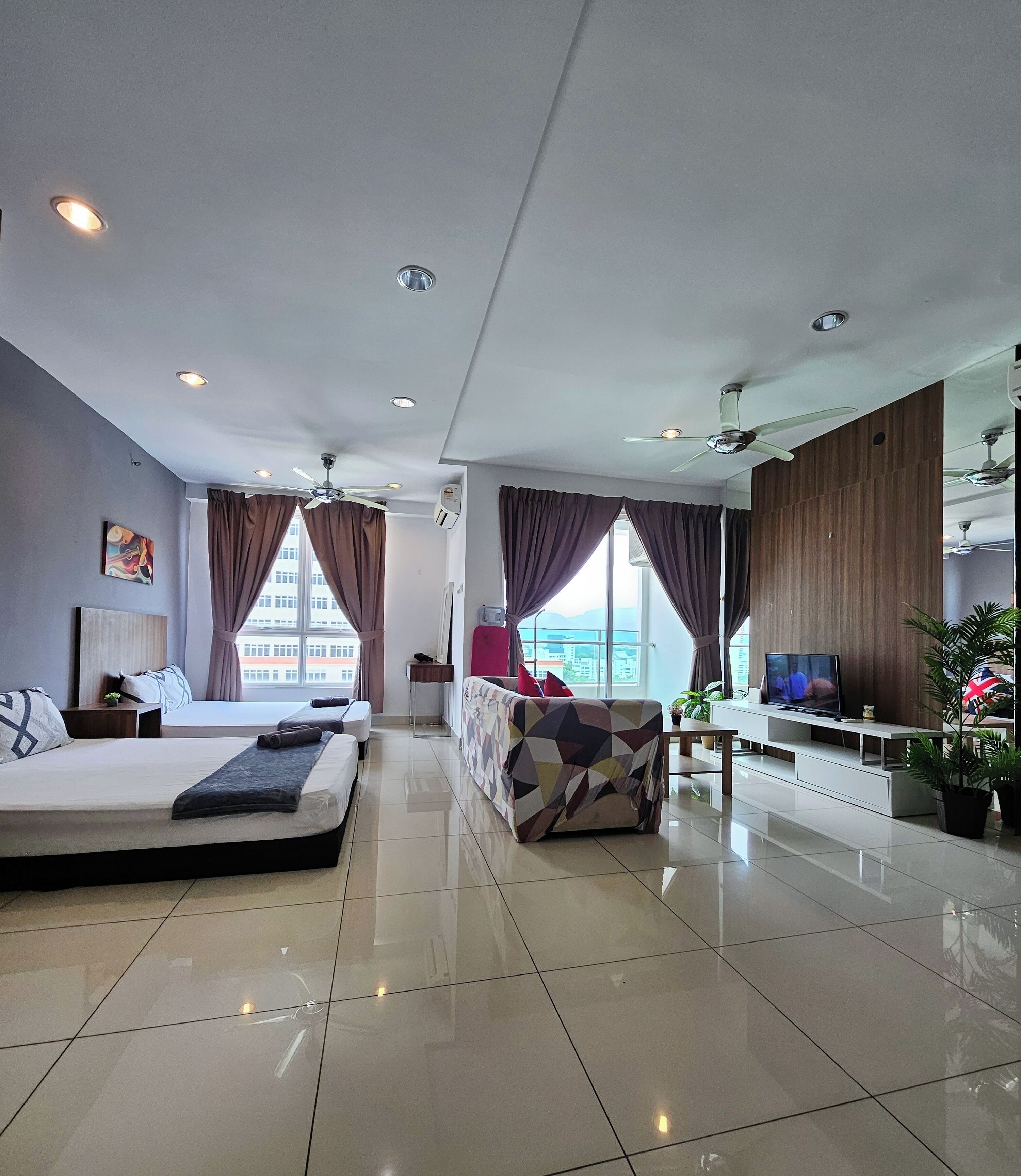 A modern hotel room with a bed, a sofa, a TV, and a large window with curtains.