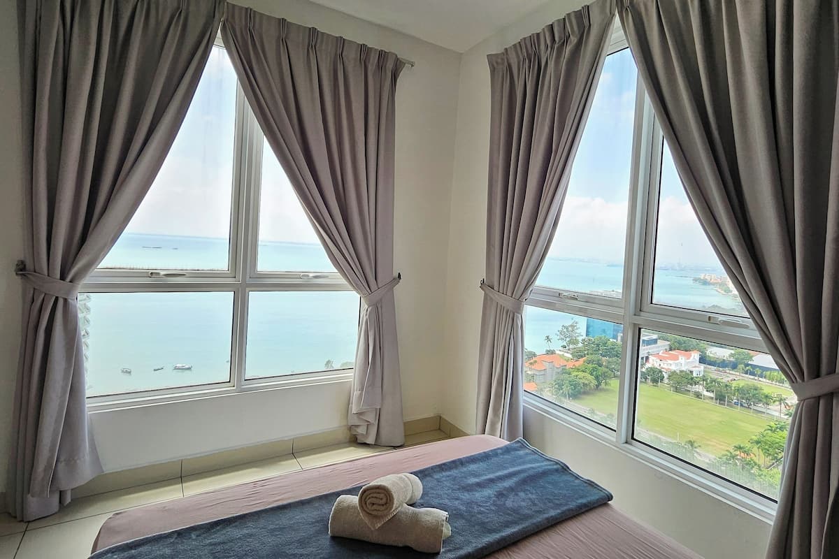Ein Zimmer mit einem Bett, einem Deckenventilator und großen Fenstern mit Vorhängen.