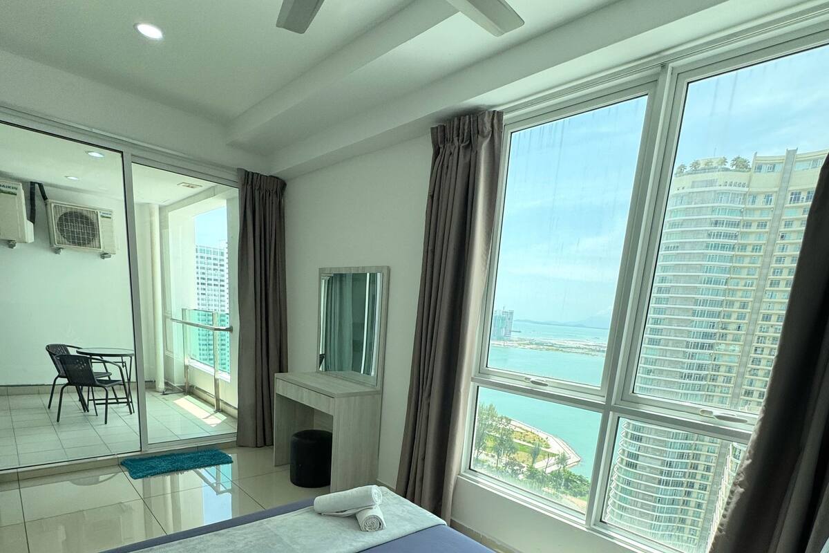 Ein Hotelzimmer mit einem großen Bett, einem Deckenventilator, einem Balkon mit Stadtblick und einem Schreibtisch mit Stuhl.