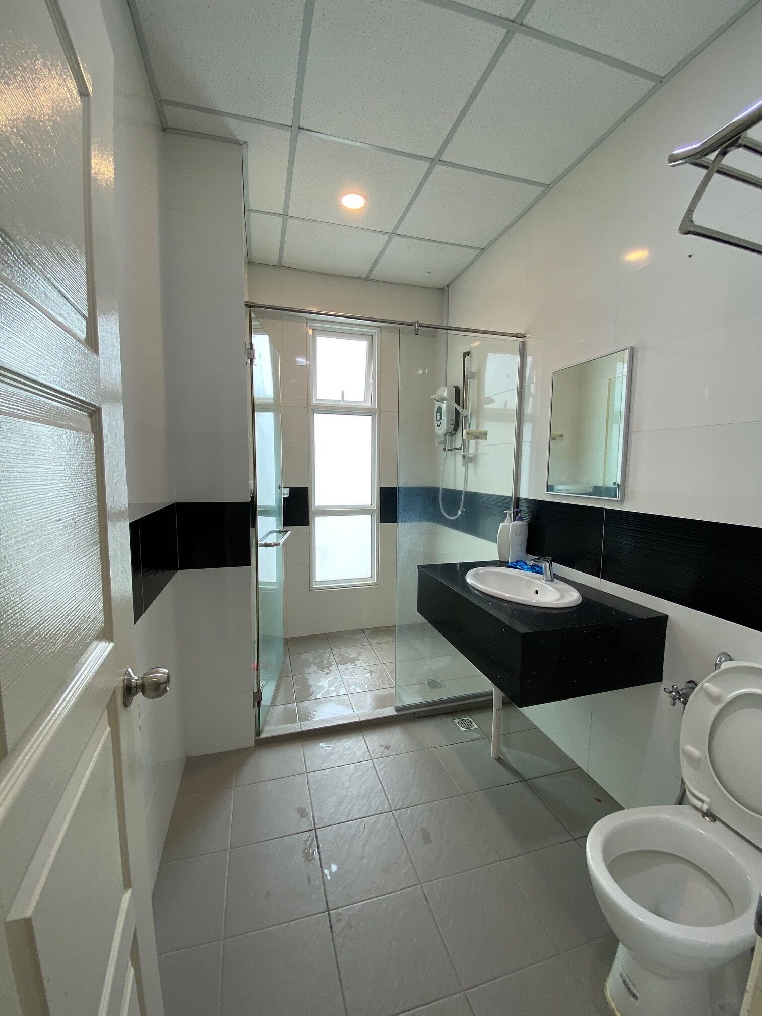 A bathroom with a glass shower enclosure, a white toilet, and a black sink with a mirror above it.