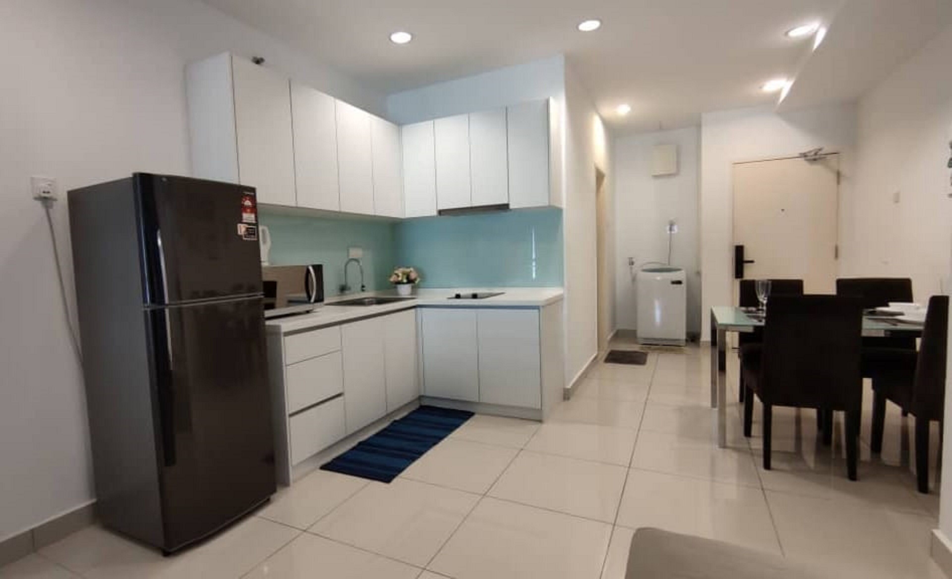 A compact kitchen with white cabinets, a black refrigerator, a sink, and a dining area with a table and chairs.