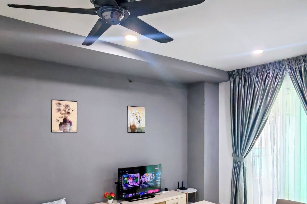 Ein modernes Wohnzimmer mit Bett, Sofa, Fernseher, Deckenventilator und Kunstwerken an den Wänden.