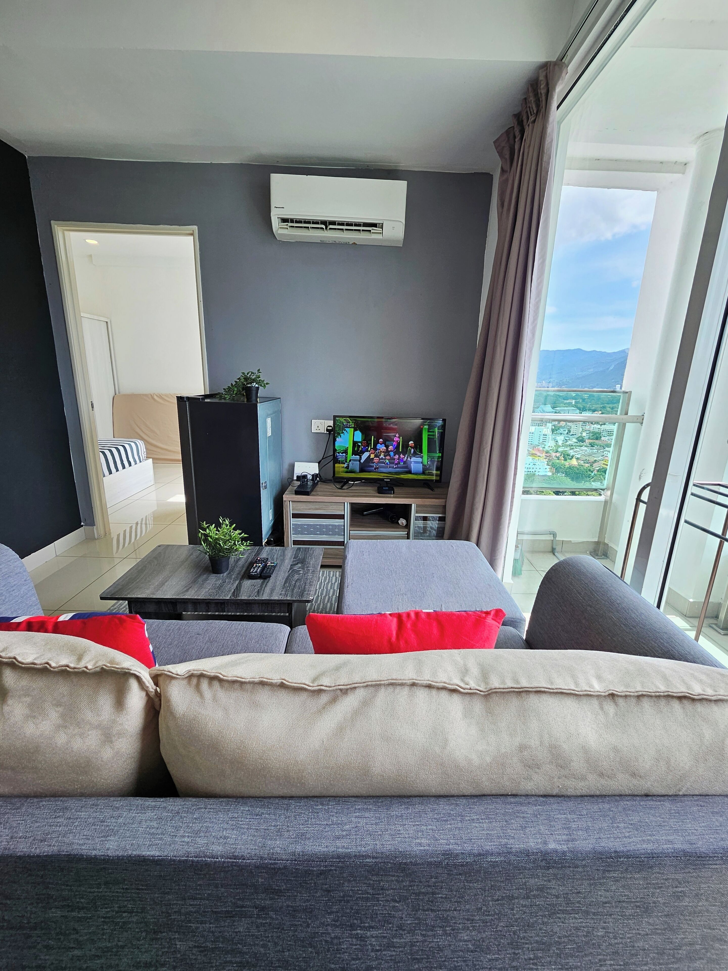 Uma sala de estar moderna com sofá, televisão de tela plana, mesa de centro e varanda com vista para a cidade.