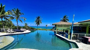 Una piscina con lettini, palme e vista sull'oceano.
