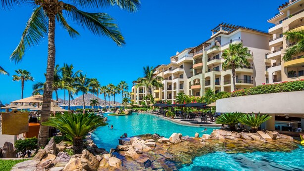 A resort with a large pool surrounded by palm trees and a multi-story building with balconies.