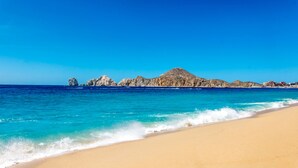 A beach with clear turquoise water, a sandy shore, and rocky formations in the background.