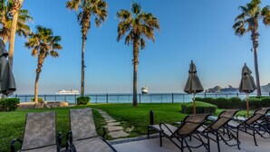 A seaside patio with lounge chairs and umbrellas, a clear view of the ocean, and a cruise ship in the distance.
