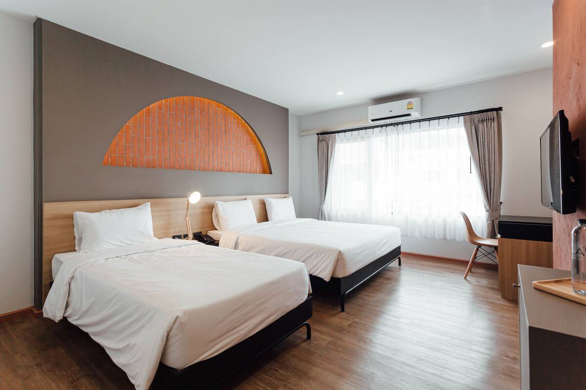 Hotellihuone, jossa on kaksi sänkyä, televisio, työpöytä ja suuri ikkuna, jossa on verhot.