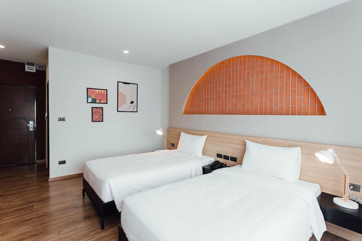 Hotellihuone, jossa on kaksi sänkyä, puinen pääty ja seinälle asennettu kaari sekä taideteoksia.