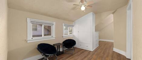 A room with wooden flooring, two black chairs, a white wardrobe, and a ceiling fan.