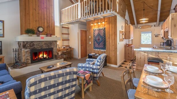 A cozy living room with a fireplace, a dining area with a table set for two, and a kitchen area. - Cute condo w/fireplace, private decks & community pool/hot tub/sauna - Cozy Curley Bear Condo (Big Sky)