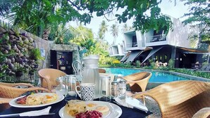 An outdoor dining area with wicker chairs and a table set for breakfast. There is a pool in the background. - Mahi Mahi Dive Resort (Zamboanguita)