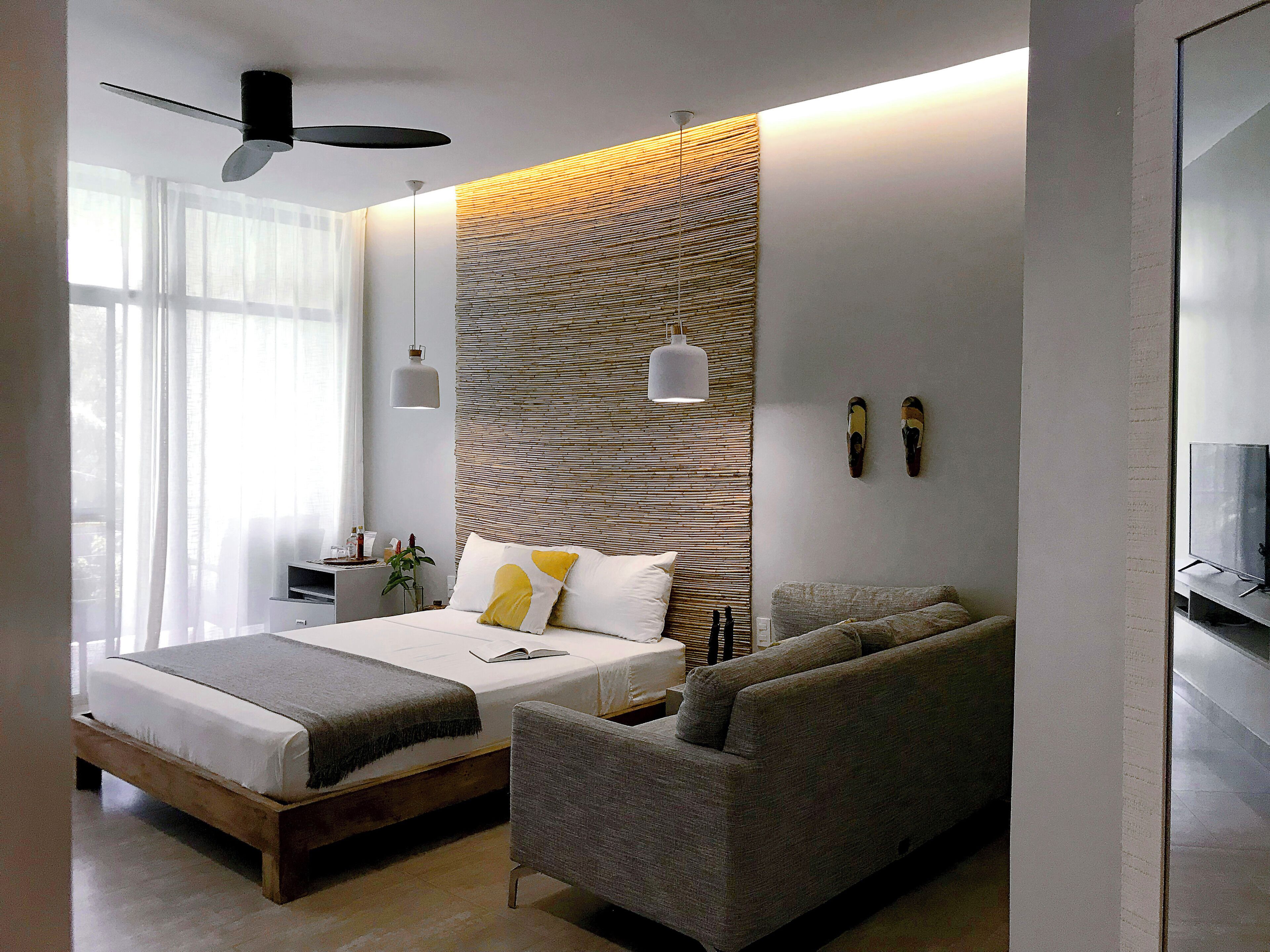 A modern bedroom with a bed, a sofa, a ceiling fan, and a wall-mounted light fixture.