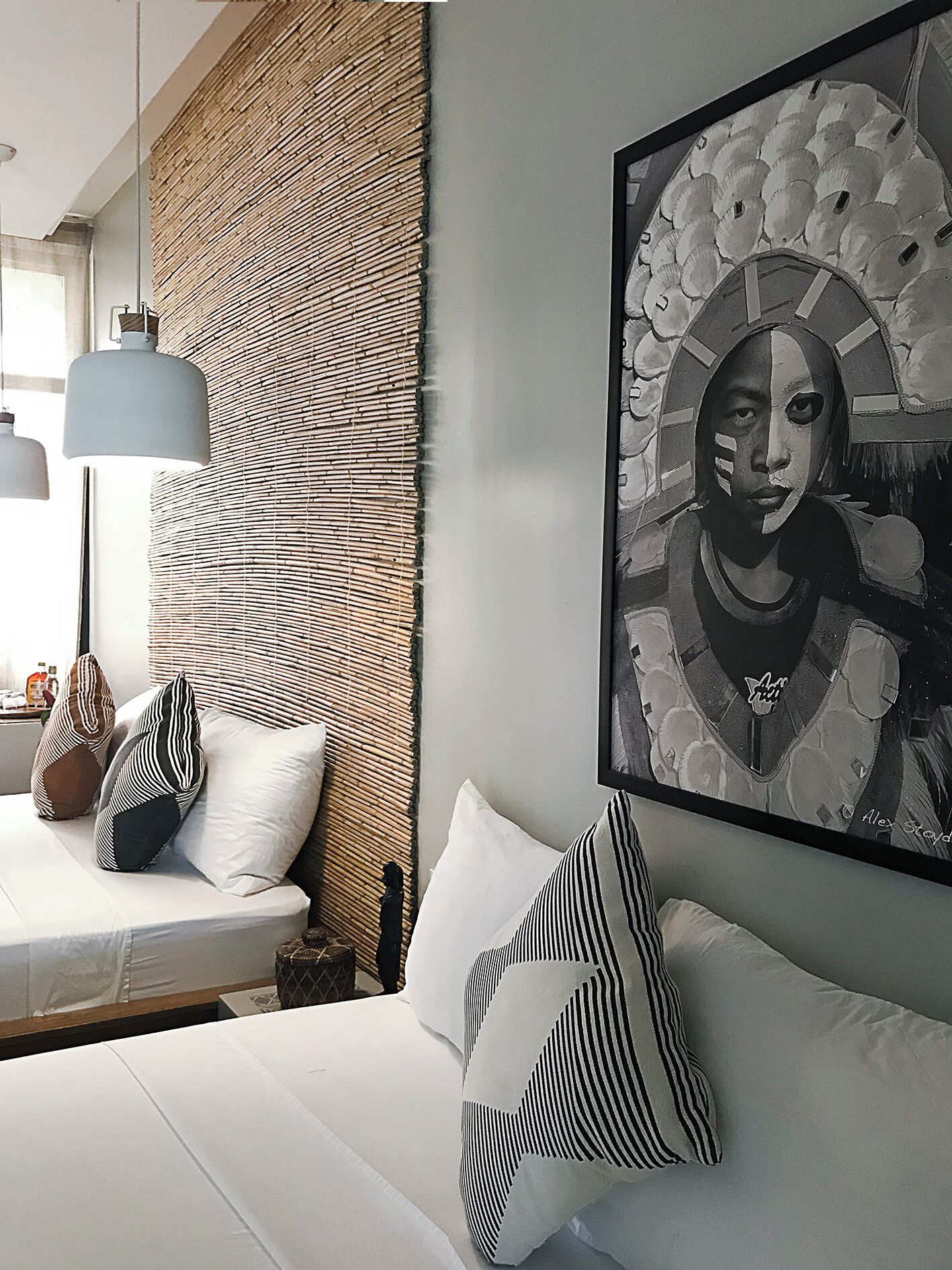Une chambre à coucher moderne avec un lit, des oreillers, une œuvre d’art accrochée au mur et une tête de lit en osier.