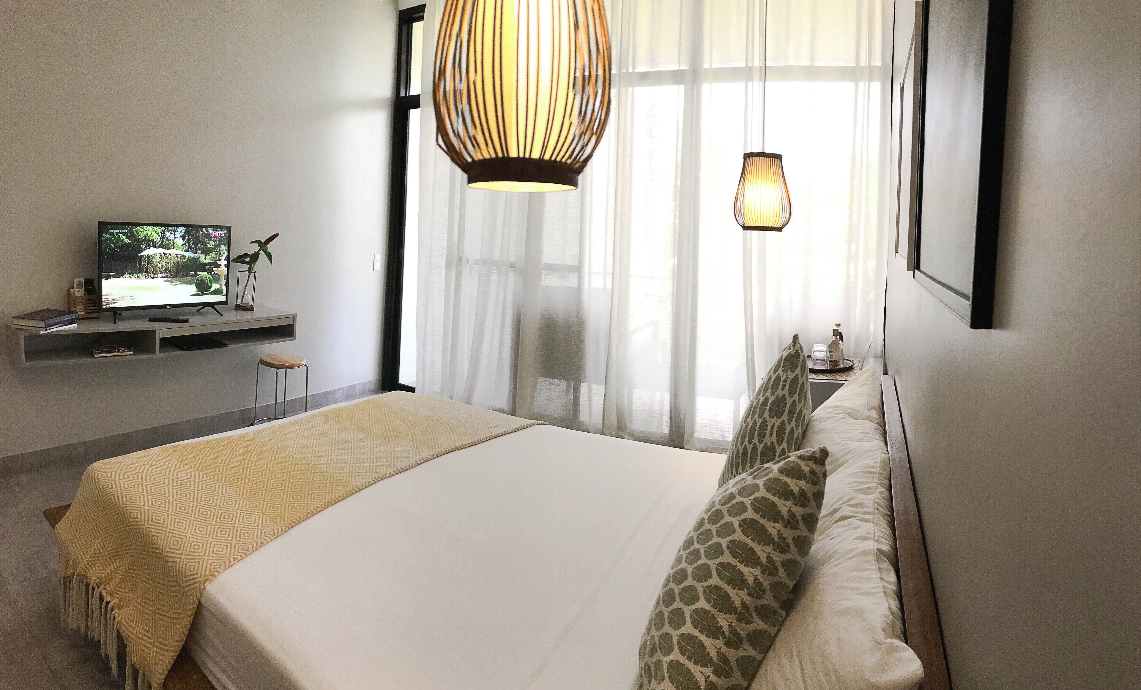 Habitación de hotel con cama, televisión, escritorio con computadora y ventana con cortinas.