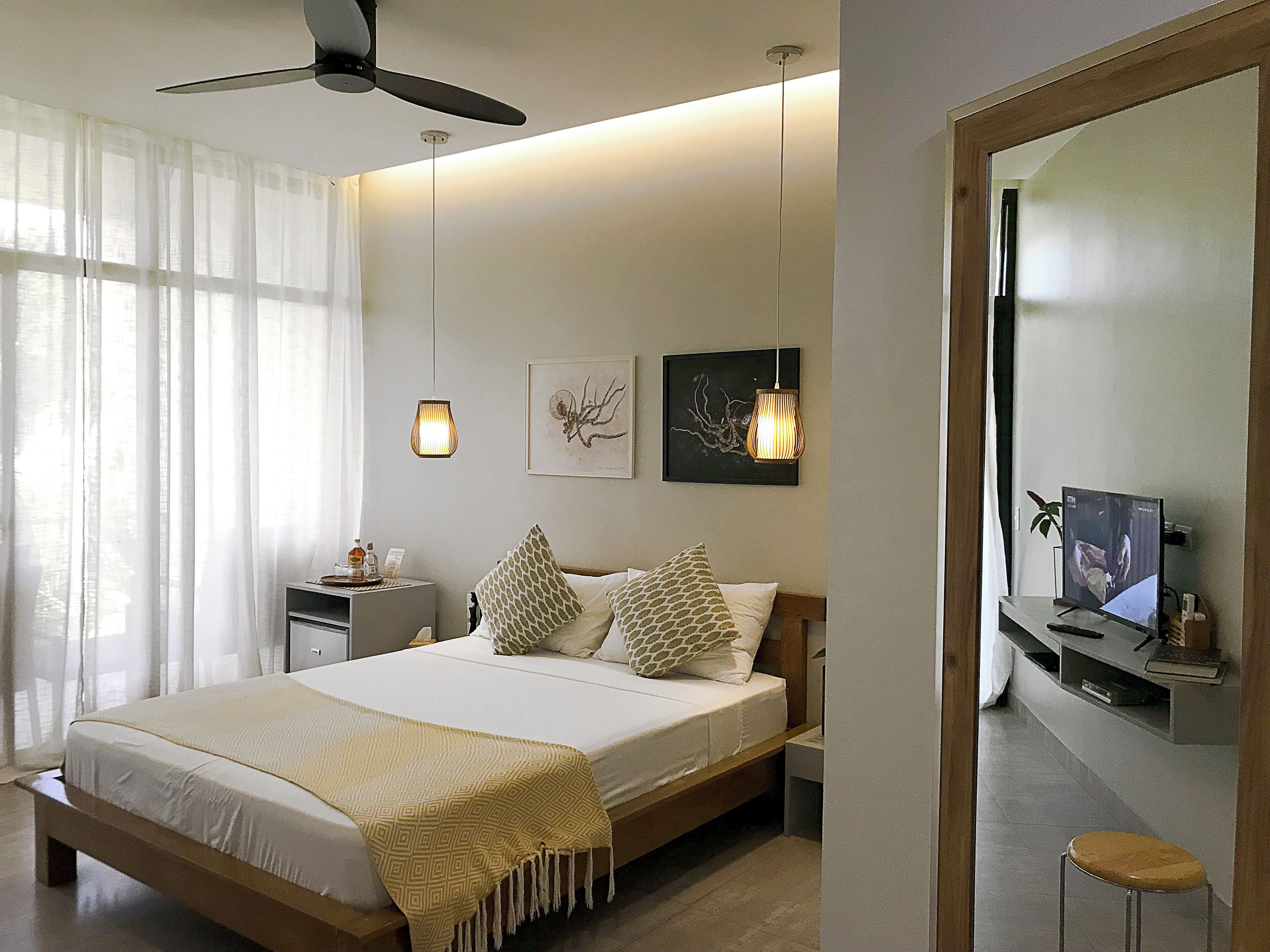 A modern bedroom with a bed, bedside tables, a ceiling fan, wall art, and a TV.