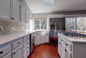 A kitchen with white cabinetry, a stainless steel refrigerator, a gas stove, and a window providing a view of the outdoors. - Renovated Portland Single Story Home- Wine Country, Amaterra, Nike, Zoo, Intel (Portland)