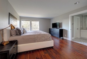 A bedroom with a bed, a dresser, a television, and a door leading to a bathroom. - Renovated Portland Single Story Home- Wine Country, Amaterra, Nike, Zoo, Intel (Portland)
