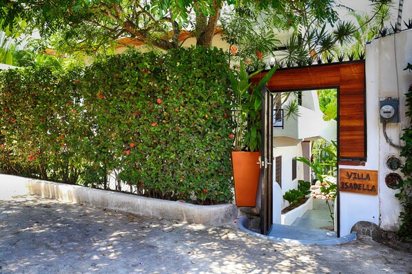 Una villa llamada "Villa Isabella" con entrada de madera, un camino de concreto y exuberante vegetación.