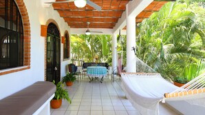 Une terrasse couverte avec un hamac, des sièges et des plantes en pot.