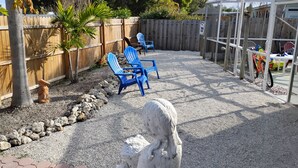 Un jardin avec une clôture en bois, des chaises bleues, une sculpture en pierre et un chemin de gravier.