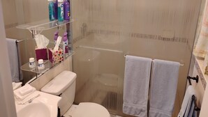 Une salle de bain moderne avec une douche à parois de verre, des toilettes et un lavabo. On trouve des articles de toilette sur une étagère et deux serviettes suspendues à un porte-serviettes.