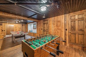 Une pièce aux murs en bois, avec une table de baby-foot et une table de billard.