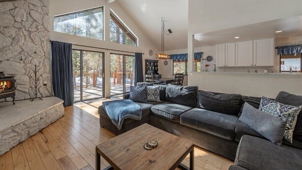 Uma sala de estar ampla com lareira de pedra, um sofá modular cinza grande e uma mesa de centro de madeira.