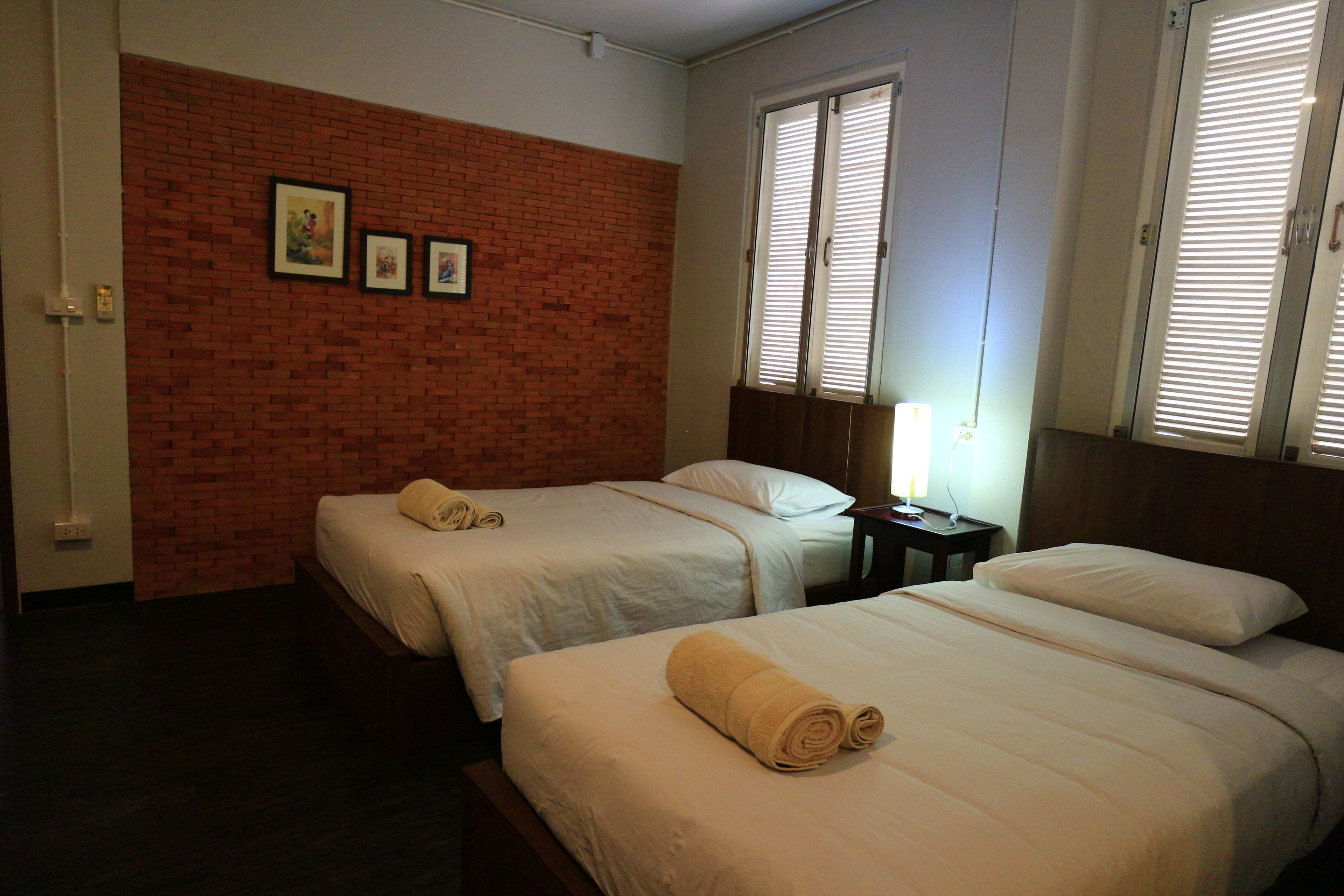 A hotel room with two beds, a brick accent wall, and a window with blinds.