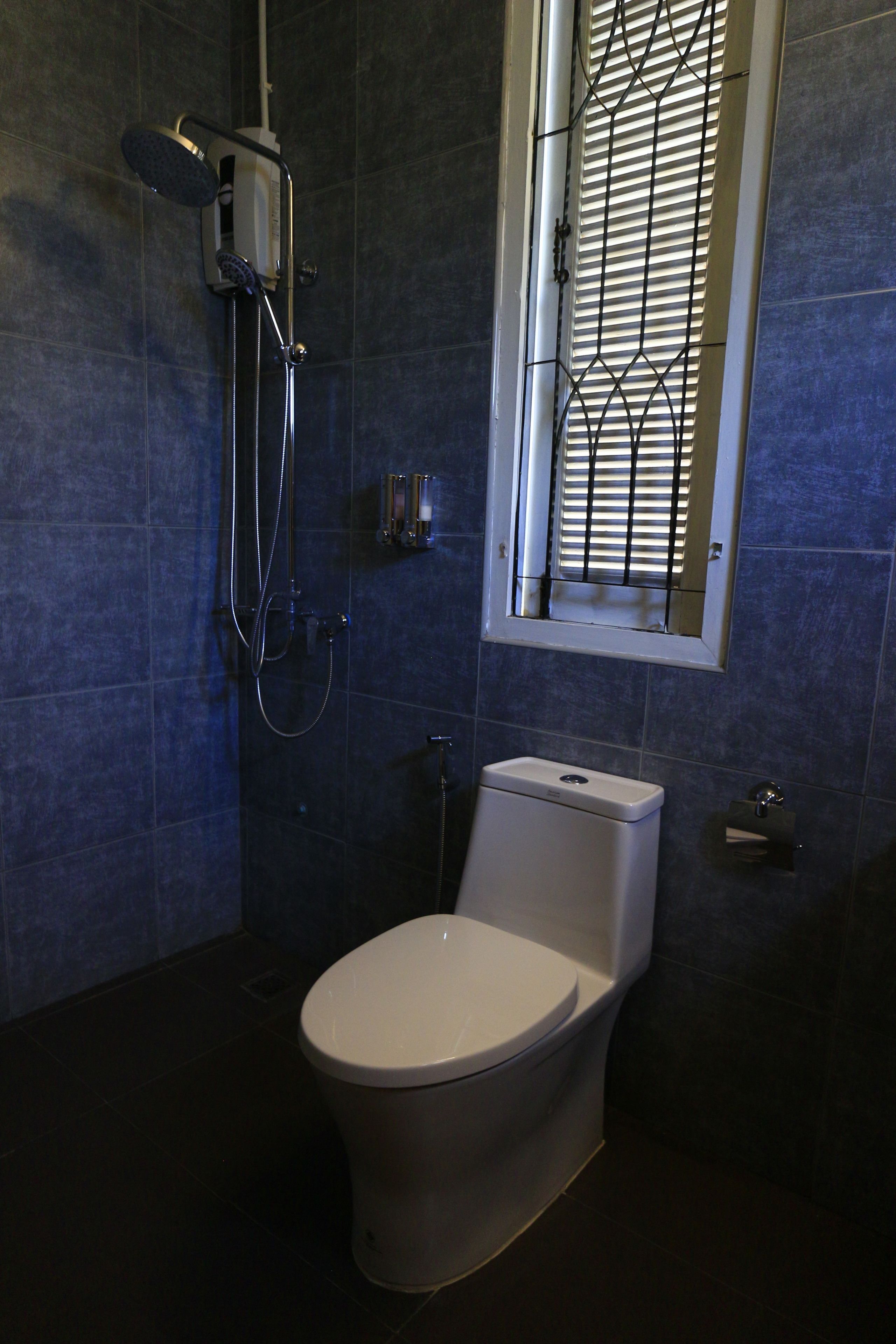 A bathroom with a toilet, a shower unit, and a window with blinds.