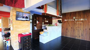 A reception area with a television displaying a news program, a reception desk, and a wooden wall with the name "BOTANIC GARDEN".