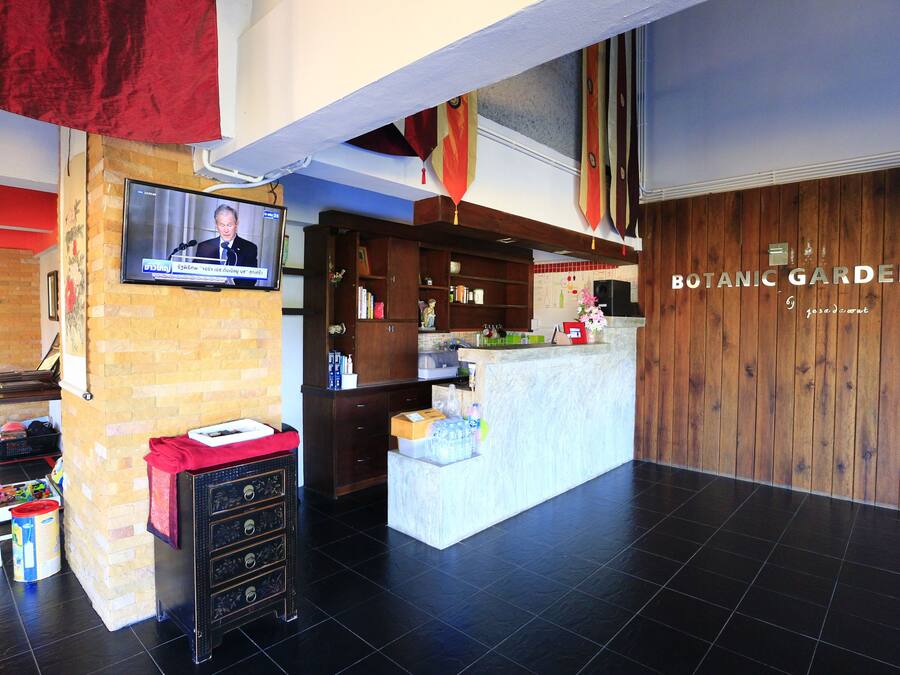 A reception area with a television displaying a news program, a reception desk, and a wooden wall with the name "BOTANIC GARDEN".