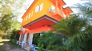 A two-story building with a bright orange facade, a balcony, and surrounding greenery. - Botanic Garden Nan Guest House (Pua)