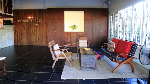 A lobby with a wooden reception desk, a seating area with a sofa and chairs, a small table, and a fan. - Botanic Garden Nan Guest House (Pua)