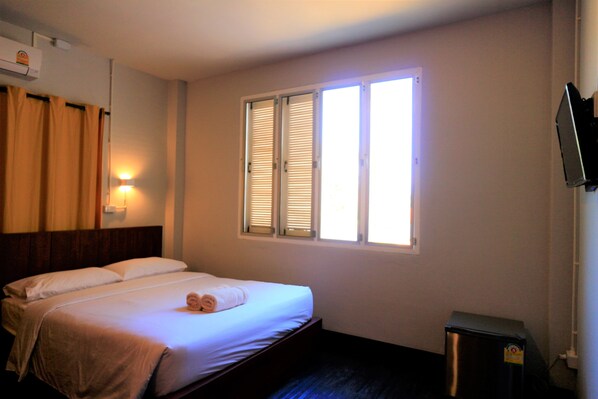 Quarto de hotel com cama, janela com persianas, televisão na parede e lixeira.