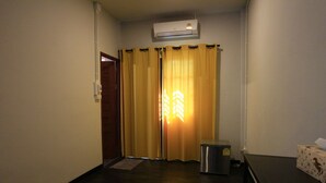 A hotel room with a wooden floor, a small trash bin, a desk with a tissue box, and a curtain blocking the view. - Botanic Garden Nan Guest House (Pua)