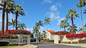 A hotel entrance with palm trees and red flowers, a clear blue sky, and a sign reading "The Palms". -  Beautiful, Palms At Wailea Condo #608- 2BR/2BA,GREAT LOCATION! SPECIAL Rates (Wailea)