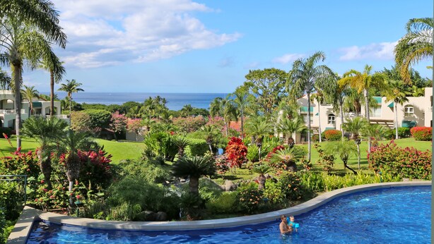 A pool area with a view of the ocean, surrounded by lush greenery and palm trees. -  Beautiful, Palms At Wailea Condo #608- 2BR/2BA,GREAT LOCATION! SPECIAL Rates (Wailea)