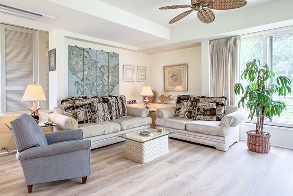 Una sala de estar con un sofá, una mesa de centro, una silla y un ventanal con cortinas.